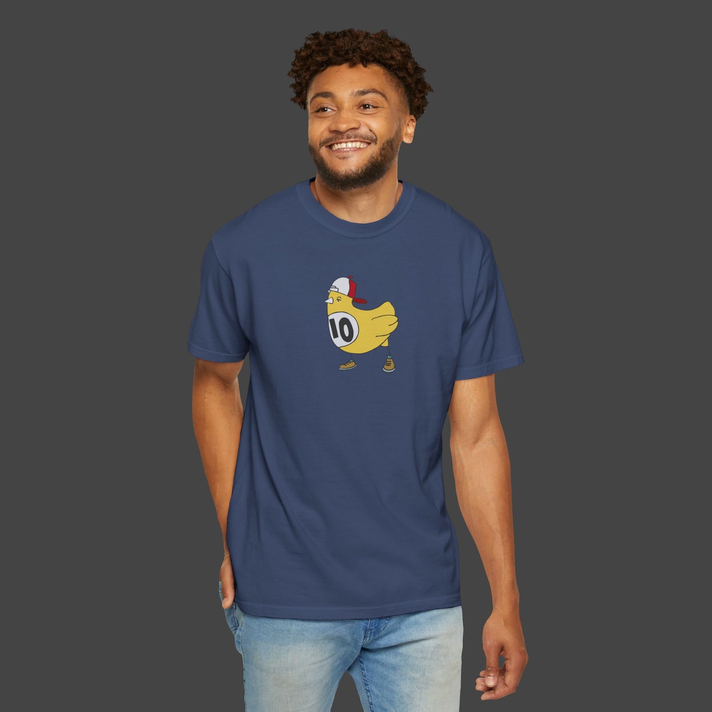 A smiling man wears the Chicken Scratch Unisex T-shirt by Jarrod Eastman from Printify. This surreal, fun blue tee shows a cartoon chicken runner in a red headband, sneakers, and race bib 10 against a dark background.