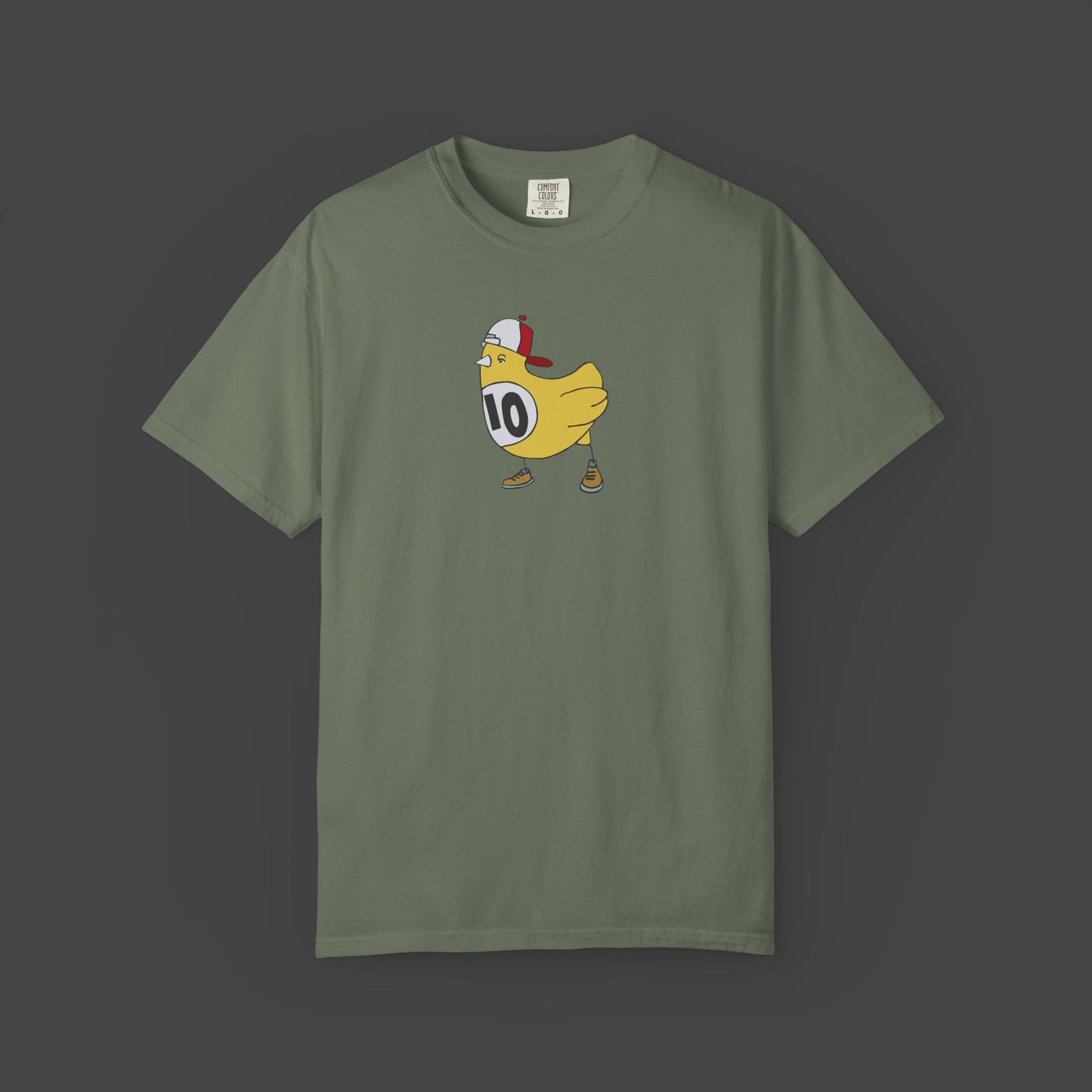 The Chicken Scratch Unisex T-shirt by Jarrod Eastman from Printify is an olive green, garment-dyed tee featuring a surreal cartoon yellow chicken in a red cap and brown shoes, wearing a white bib with the number 10 on a dark background.