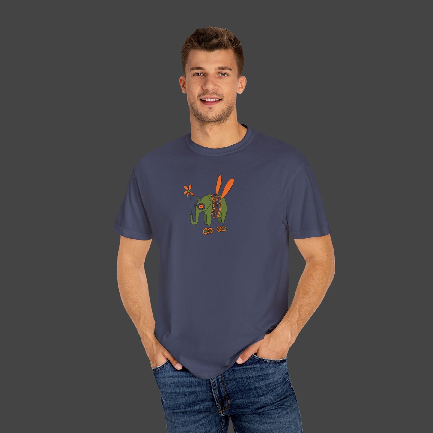 A smiling man wears the Flying Elephant Unisex T-shirt by Printify, designed by Jarrod Eastman, featuring a colorful cartoon elephant, standing with hands in pockets against a plain gray background.
