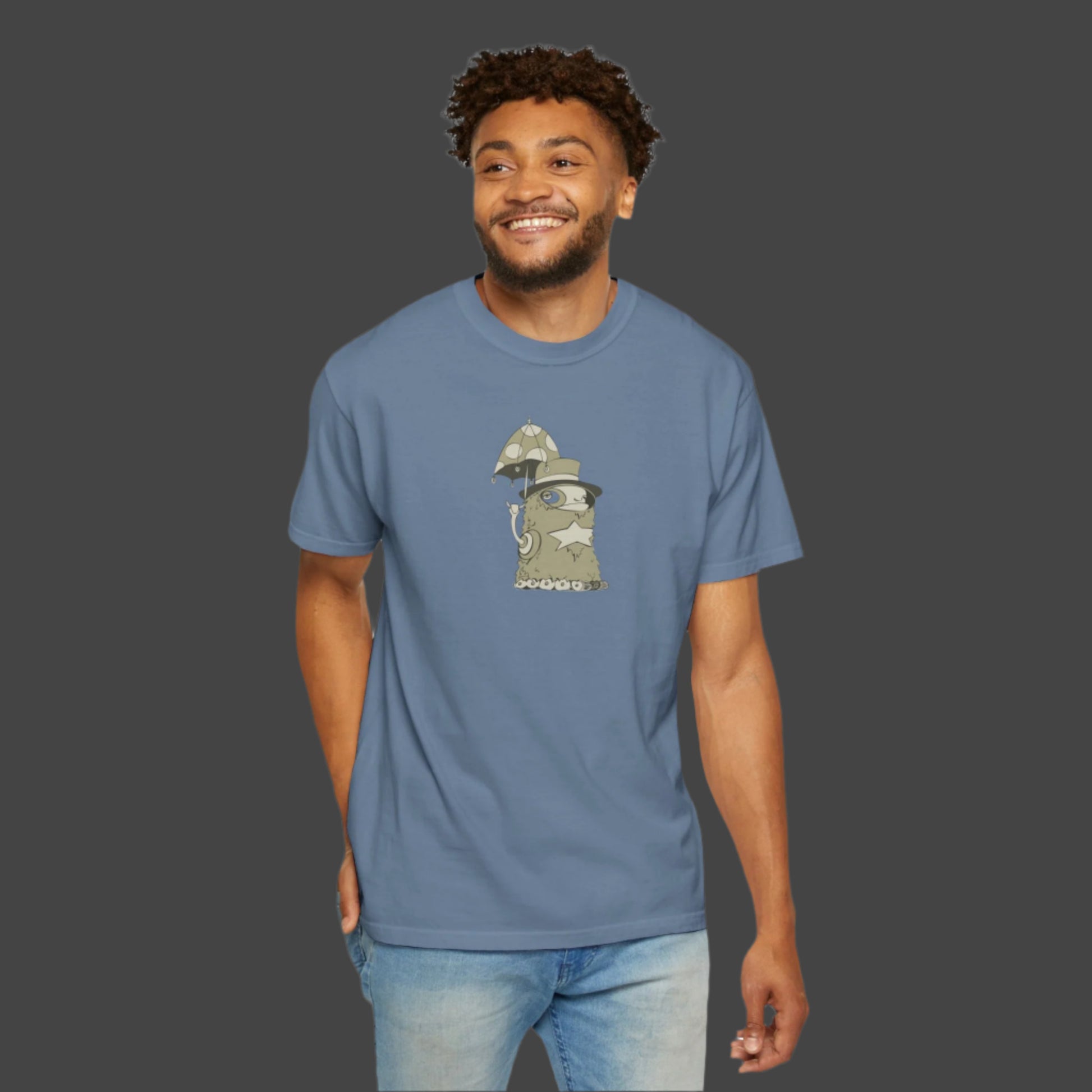 A man wears the Funky Monster T-shirt by Printify, featuring Uptown Lester’s whimsical wizard cat with a mushroom staff beside a large mushroom. He smiles, one hand in his pocket.