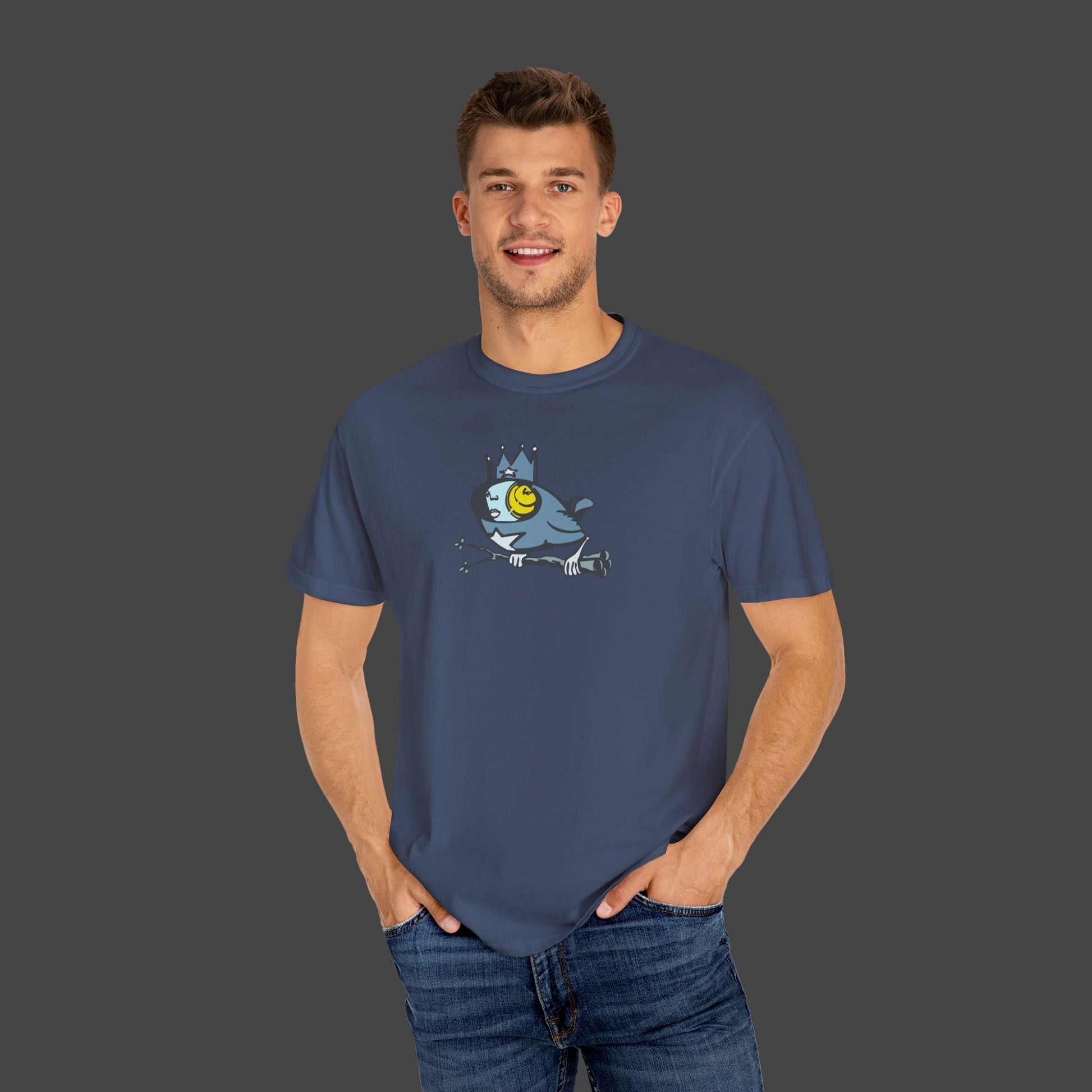 A smiling man stands against a gray background with his hands in his pockets, wearing the Biddy Surreal Bird Unisex T-shirt by Jarrod Eastman