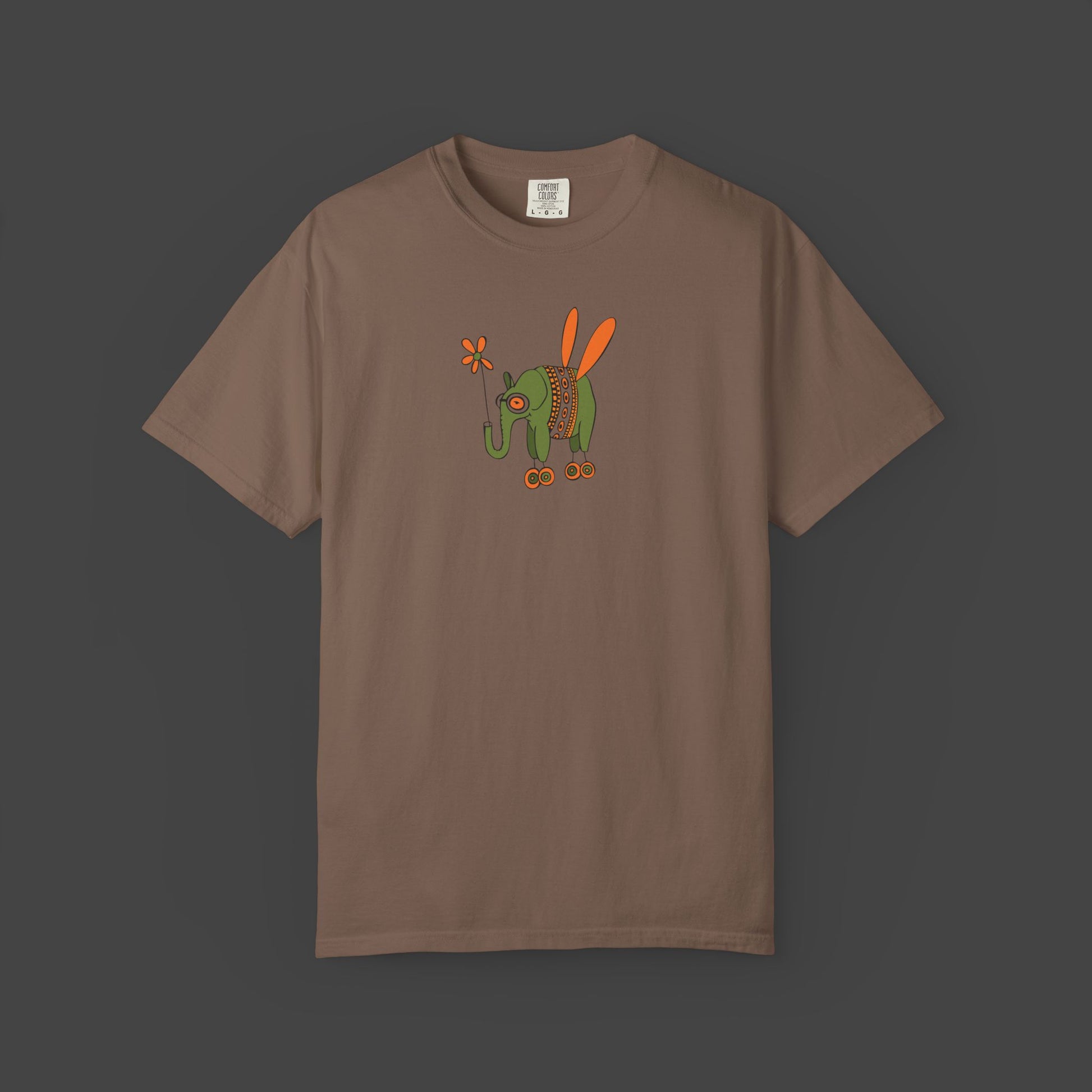 The Flying Elephant Unisex T-shirt by Printify features Jarrod Eastmans whimsical green elephant with orange wings and flower on a garment-dyed shirt—a vibrant, inspirational look perfect for art lovers.