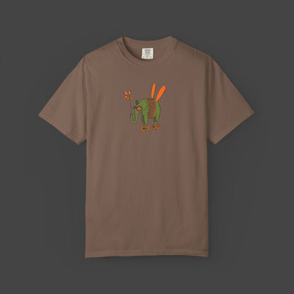 The Flying Elephant Unisex T-shirt by Printify features Jarrod Eastmans whimsical green elephant with orange wings and flower on a garment-dyed shirt—a vibrant, inspirational look perfect for art lovers.