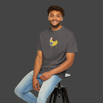 A smiling man sits on a stool against a gray backdrop, wearing Printifys Chicken Scratch Unisex T-shirt by Jarrod Eastman—a surreal and fun top with a cartoon duck in a red cap and jersey 10—paired with light blue jeans.
