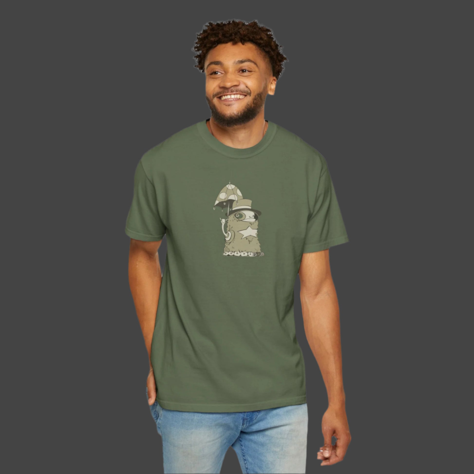 A smiling man in light blue jeans and short curly hair shows off his artistic flair in the Funky Monster T-shirt – Uptown Lester Design by Printify, featuring a whimsical cartoon cat in a wizard hat standing beside two mushrooms.