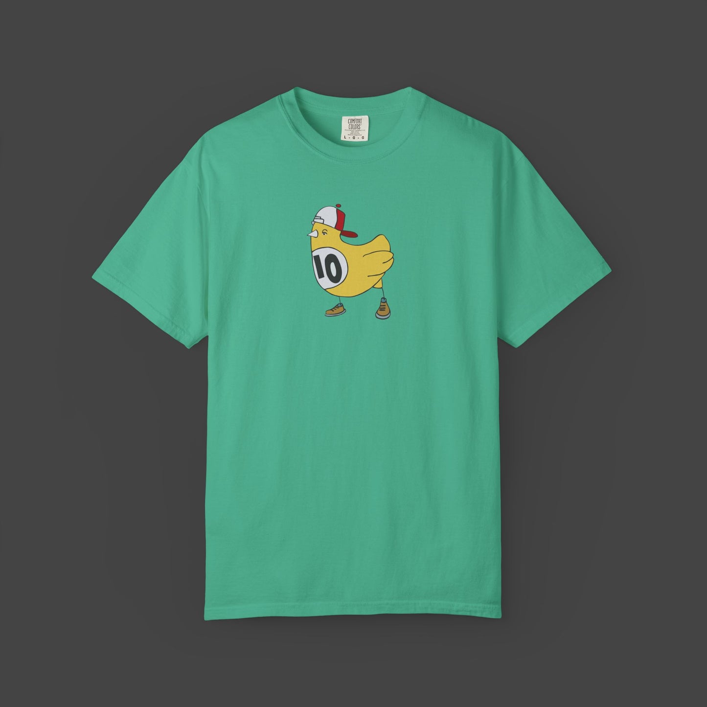The Chicken Scratch Unisex T-shirt by Jarrod Eastman (Printify) features a surreal design: a cartoon yellow chicken in sneakers, red-and-white cap, and bib #10, boldly printed at the center. Fun, quirky art style on this green garment-dyed tee.