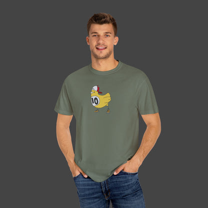 A smiling man wears the Chicken Scratch Unisex T-shirt by Jarrod Eastman from Printify—a green tee with a surreal cartoon duck in a helmet and number 10 jersey—standing hands-in-pockets before a plain gray background.