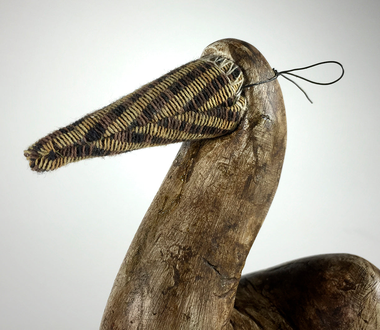 The Bob by jarrodeastman is a wooden bird sculpture featuring a long beak wrapped in patterned fabric and finished with a thin black cord, set against a plain light background.