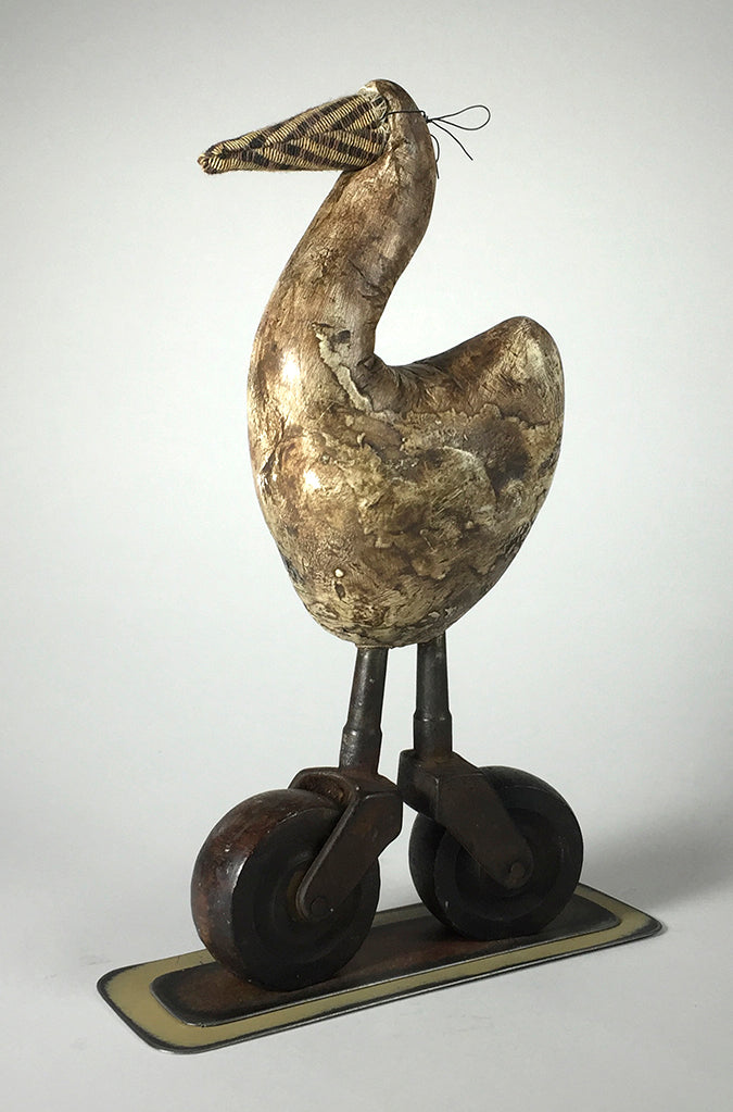 Bob by jarrodeastman is a wooden bird-like sculpture with a textured body, wire-wrapped long beak, and metal legs on antique castor wheels, standing on a rectangular base.