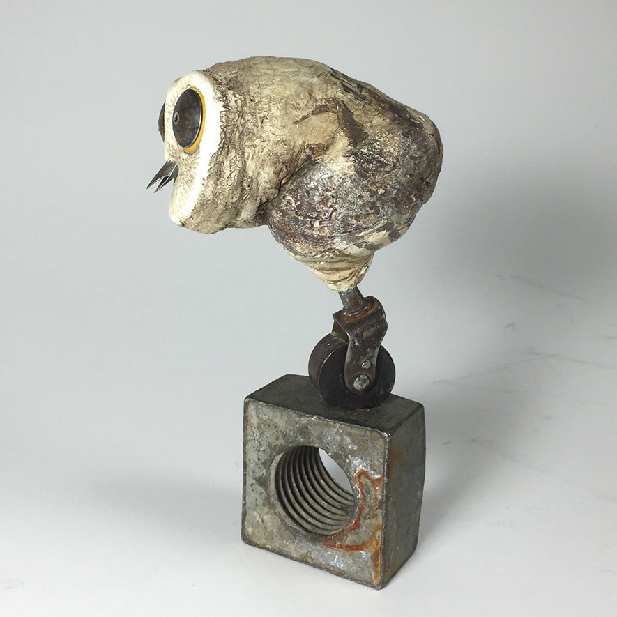 The Owl by jarrodeastman is a sculpture of a bird with a textured, stone-like body, perched on a metal wheel top of a rusted block, featuring prominent beak and eyes.