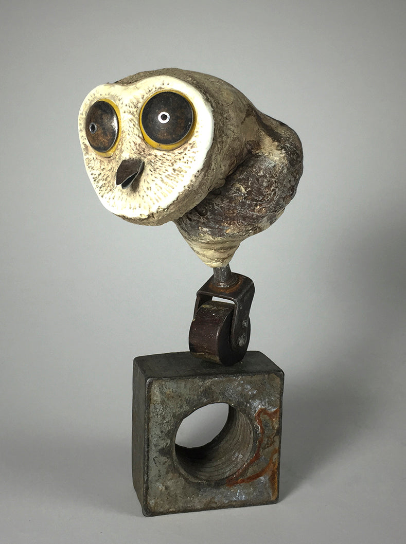 The Owl by jarrodeastman is a whimsical stone and metal sculpture featuring large round eyes, a beak, and a white textured head. It stands on a square metal base with a circular hole, adding unique charm to any space.