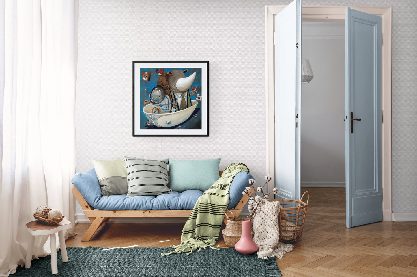 A cozy living room features a light wooden sofa with pastel cushions, a green blanket, and Preaching to the Choir wall art by Prodigi above. An open door reveals another room; baskets and decor decorate the wooden floor.