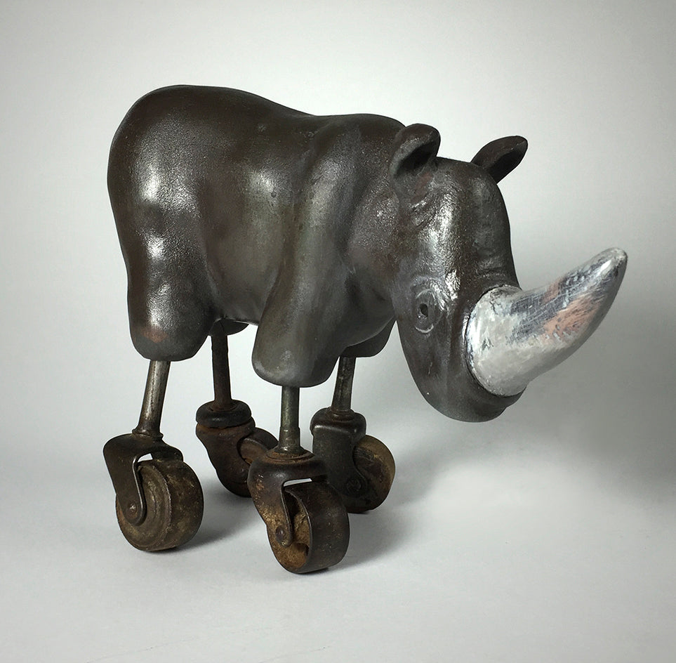 Rhino by jarrodeastman is a polymer clay sculpture of a rhinoceros with four castor wheels for legs, metallic finish, and prominent horn, displayed against a plain gray background.