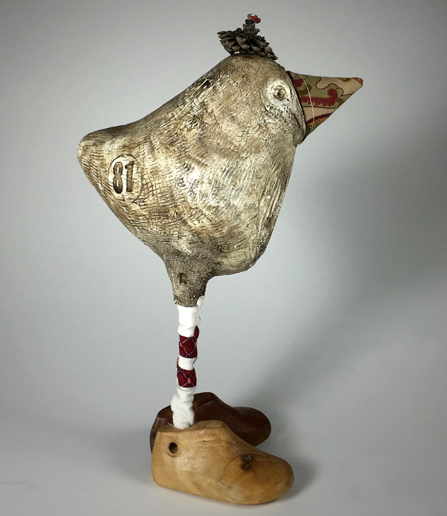 Tweeter by jarrodeastman is a whimsical bird sculpture with a textured body, red-and-white striped legs, wooden shoe feet, a small hat, patterned cone-shaped beak, and the number 81 on its side.