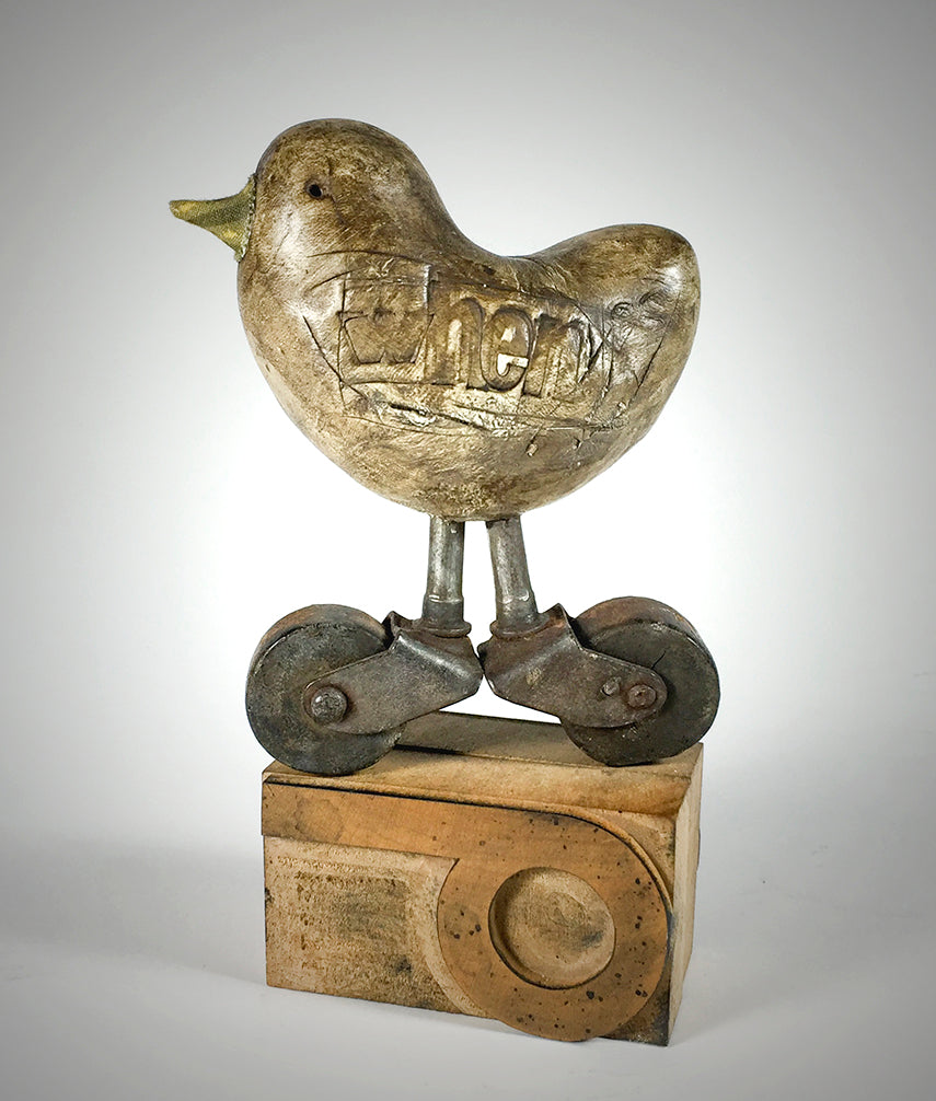 Whenever by jarrodeastman: a small polymer clay bird with cheer carved on its side, set on antique castor wheels and mounted on a wooden block with a circular groove.