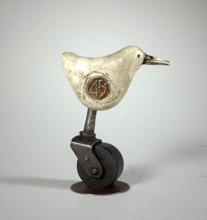 Why by jarrodeastman: a small original polymer clay sculpture of a white bird with an orange 45 on its side, standing on an antique castor wheel, displayed against a plain gray background.
