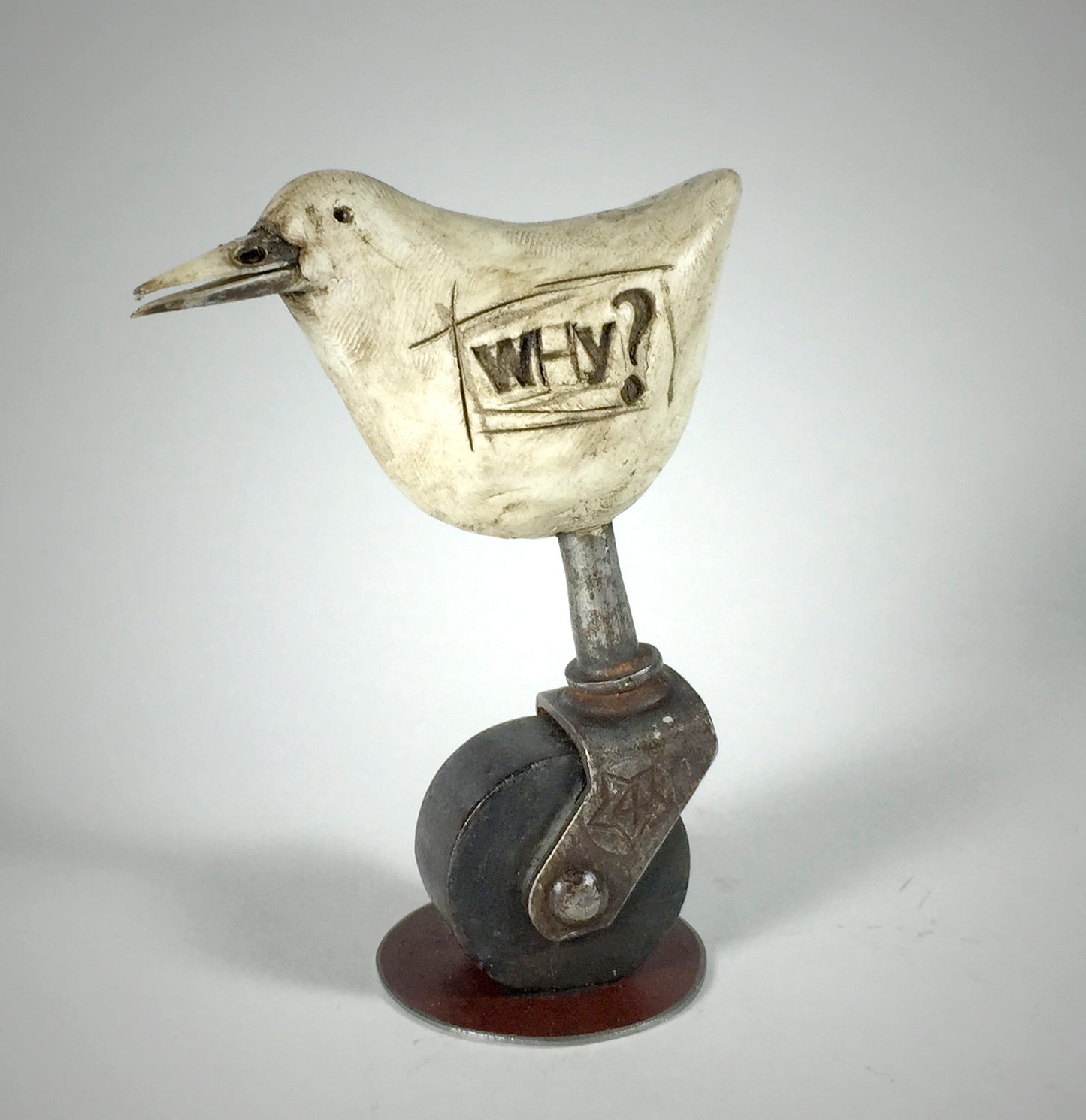 “Why” by jarrodeastman is an original whimsical bird sculpture with WHY? carved on its side, perched atop an antique castor wheel that combines playful and industrial styles.