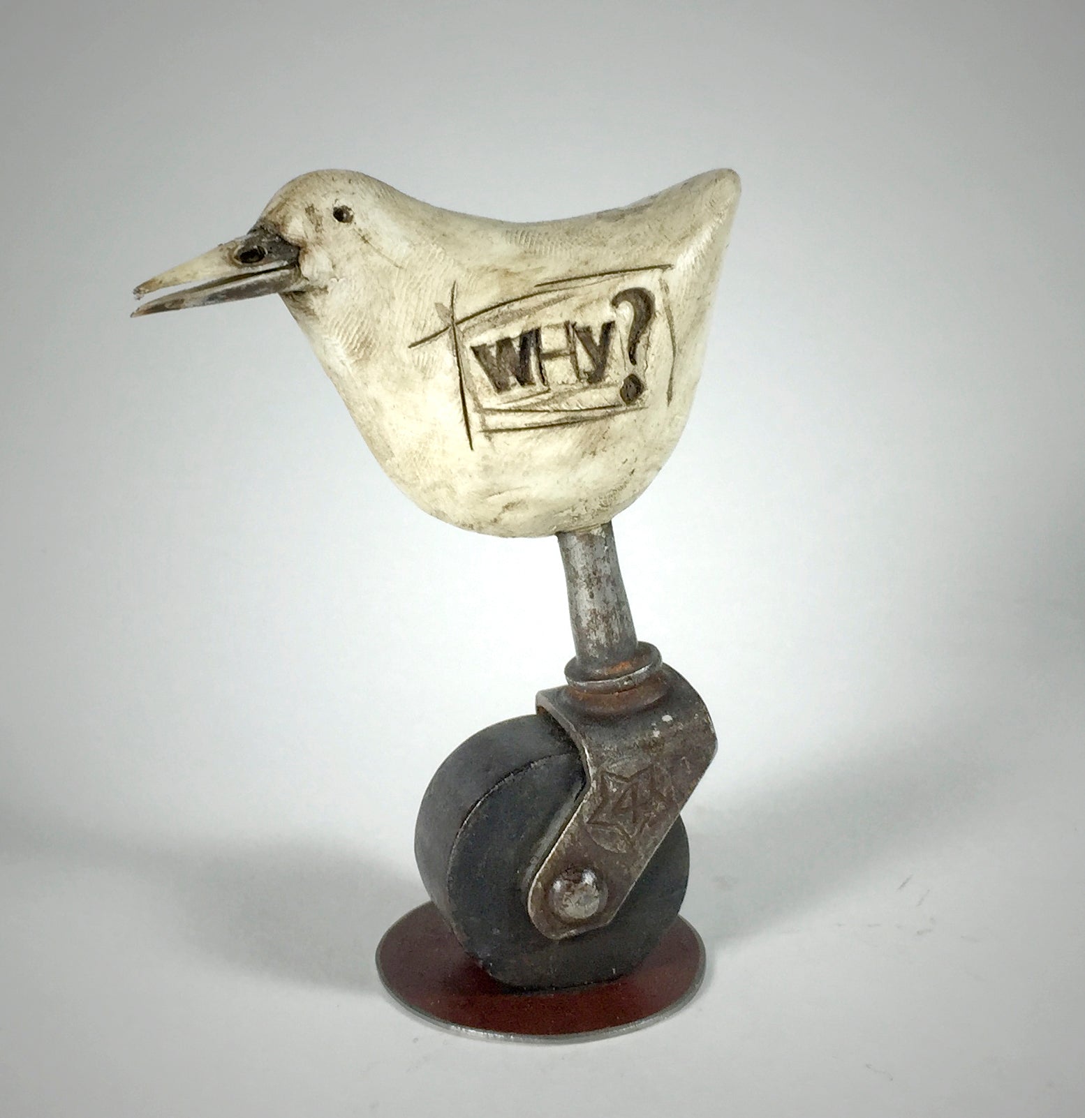 “Why” by jarrodeastman is an original whimsical bird sculpture with WHY? carved on its side, perched atop an antique castor wheel that combines playful and industrial styles.